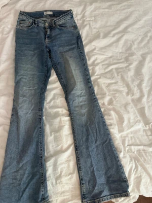 Blå bootcut jeans från ginatricot - Snygga blå bootcut jeans från ginatricot med klassisk femficksdesign och lätt slitning framtill. Jeansen har normal passform och är tillverkade i mjukt denimtyg som ger en skön känsla. Perfekta för dig som gillar en tidlös och avslappnad stil.