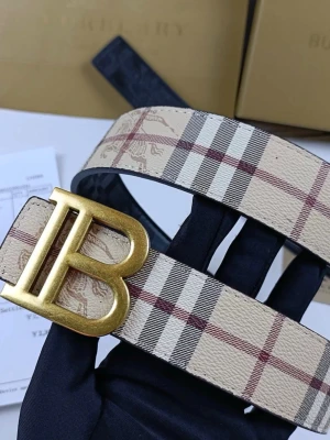 Burberry rutigt bälte med B-spänne - Snyggt bälte från Burberry med klassiskt beige, brunt och rött rutmönster. Bältet har ett stort guldfärgat B-spänne och är gjort i läder med präglad logga. Perfekt accessoar för att lyfta din outfit. Box följer ej med.