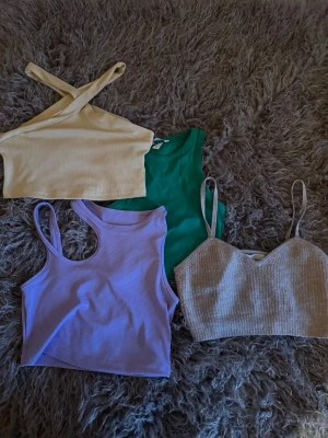 Fyra trendiga ribbade linne-toppar - Fyra snygga linne-toppar i olika färger: ljusgul med korsade axelband, grön klassisk modell, lila ribbad med breda axelband och beige ribbad med tunna axelband och v-ringning. Perfekta för att mixa och matcha till olika outfits.