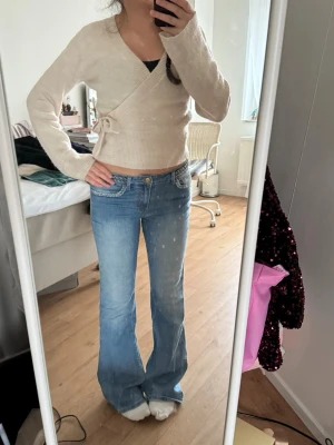 Ljusblå bootcut jeans med låg midja - Säljer ett par ljusblå bootcut jeans med låg/mid midja och klassiska fem fickor. Jeansen har en snygg tvätt och subtila slitningar för en avslappnad look. Perfekta för dig som gillar en retro vibe och vill ha ett par jeans som sticker ut. Storlek M men passar på S. 