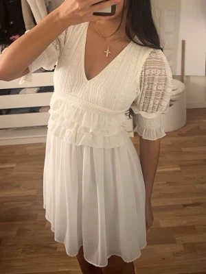 Student klänning  - Supersöt vit kort student klänning med v-ringning, volangdetaljer och puffiga spetsärmar. Denna klänning finns inte längre att köpa och är bara använd en gång😊 detta är en storlek 34 men är lite insydd så lutar nu lite mer till en 32 skulle jag säga. Vid insidan av klänningen har den en liten smink fläck men detta är inget som syns när klänning är på🩷☺️