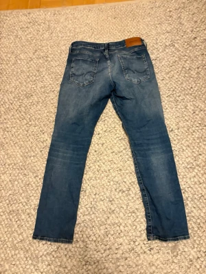 Blå jeans från Jack & Jones - Snygga blå jeans från Jack & Jones med klassisk femficksdesign och raka ben. Jeansen har en ljus tvätt och är tillverkade i bomullsmix för skön känsla. Perfekta för en avslappnad och trendig stil.
