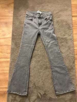 Grå bootcut jeans med hög midja - Snygga grå jeans med bootcut-modell och hög midja. Klassisk femficksdesign och raka sömmar. Perfekta för dig som vill ha en retroinspirerad look med lite utsvängda ben. Tillverkade i mjukt bomullsmaterial för skön känsla.
