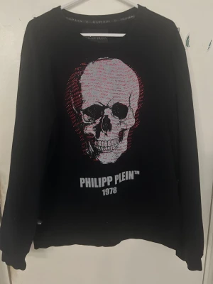 Svart sweatshirt Philipp Plein XXL - Cool svart sweatshirt från Philipp Plein med stor döskalle i rött och vitt framtill. Tröjan har rund hals och trycket är dekorerat med små glittriga detaljer. Perfekt för dig som gillar statement-plagg och streetwear.
