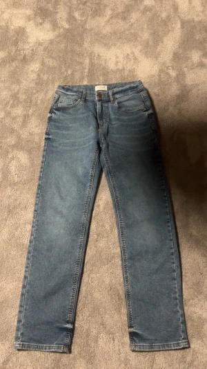 Blå jeans från Lindex, modell Staffan - Typ alldrig använda !Snygga blå jeans från Lindex, modell Staffan. Klassisk femficksdesign med raka ben och normal passform. Jeansen är tillverkade i bomull och har en ljus tvätt som ger en fräsch look. Perfekta för en avslappnad stil.
