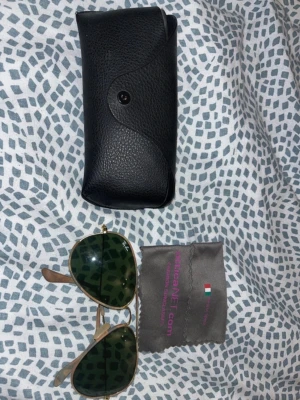 Ray-Ban Aviator solglasögon guld - Säljer ett par klassiska Ray-Ban Aviator solglasögon med guldfärgad metallbåge och gröna linser. Medföljer original svart fodral och putsduk. Perfekt accessoar för dig som vill ha en tidlös och ikonisk look.