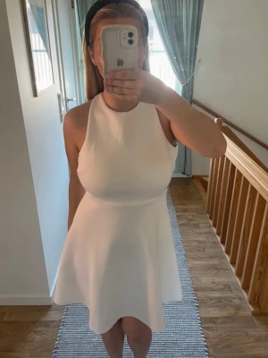 Vit ärmlös kortklänning - Säljer en stilren vit klänning med ärmlös design och rund halsringning. Klänningen har en utsvängd kjol och är perfekt för varma dagar. Enkel och snygg modell som passar till många tillfällen som student, konfirmation och skolavslutning