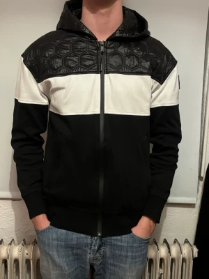 Moose knuckles - Snygg cardigan Moose Knuckles med svart och vit färgblockdesign. Överdel och huva i glansigt, quiltat material med hexagonmönster. Dragkedja framtill och ribbade muddar. Ny pris 3500kr vårt pris 799kr✅