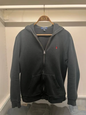 Ralph Lauren hoodie - En svart Ralph Lauren hoodie i barnstorlek XL (Motsvarar S i vuxenstorlekae) och ett okej skick därav det låga priset. Den har lite slitningar i ärmen men annars är det rätt fin. Använd ett flertal gånger man har mycket mer ätt ge, Nypris: ca 1500kr