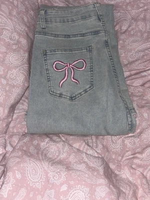 Ljusblåa jeans med rosetter - Ljusa jeans med broderade rosetter på bakfickorna, har en utsvängd passform. Endast testade och dom passade mig inte, för korta i benen men midjan satt bra. Är 1,70cm så skulle säga att nån 1,65cm skulle passa bra i dom. Obs! Ansvarar ej för postens slarv!. Storlek S/36.