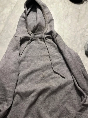 Grå merinoull hoodie  - En stilren grå hoodie med huva och dragsko. Hoodien har en klassisk passform och är tillverkad i mjukt material som känns skönt mot huden. Perfekt för en avslappnad look och enkel att matcha med andra plagg. Den är i helt okej skick förutom några smuts ”fläckar” vid luvan som säkert går bort i tvätten. Den passar perfekt runt 165cm.