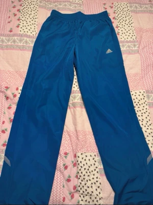 Adidas climalite tränings byxa - Blåa Adidas climalite tränings byxa.  Med reflexer längst ner på byxorna. Nere vid benen finns det band som man kan dra åt.  Storlek: M , smal passform.  Bredd på midjan är: 38cm  Bredd på låren är: 30cm  Längden : 82cm  Byxorna är i fint skick. Inga defekter , lappen på insidan har jag sen innan klippt bort för den har skavt