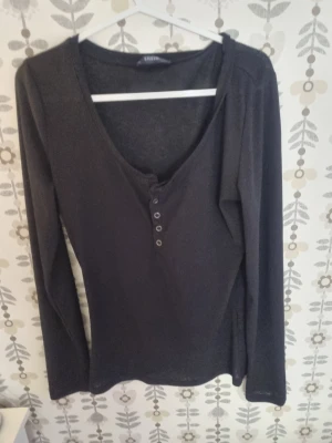 Svart långärmad topp med knappar - Svart långärmad topp från Gina Tricot med v-ringning och dekorativa knappar framtill. Enkel och stilren design som passar till många olika outfits. Mjukt material och normal passform.