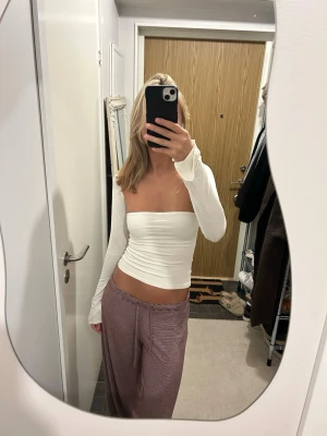 Vit långärmad offshoulder topp - Säljer en vit, långärmad topp med tight passform. Toppen är tillverkad i ett mjukt och stretchigt material som sitter snyggt mot kroppen. Perfekt för dig som gillar minimalistisk och stilren look.
