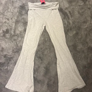 Ljusgrå bootcut byxor från edikted - Supersnygga ljusgrå bootcut byxor från edikted med bred övervikt mudd och mjukt, stretchigt material. Perfekta för en chill och trendig look. Byxorna har en skön passform och vida ben som ger en riktigt snygg siluett.