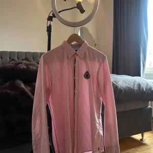 Randig skjorta från Morris Stockholm - Snygg skjorta från Morris Stockholm i vitt och rött med smala ränder. Klassisk krage, långärmad och med broderad logga på bröstet. Skjortan har knappar framtill och är tillverkad i bomull för en skön känsla.