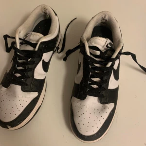 Nike panda dunk sneaker  - Använda men i relativt bra skick! Svarta och vita Nike Dunk Low sneakers med klassisk svart swoosh på sidorna. Skorna har snörning, perforerad tå och platt sula. Ovandelen är i skinn och insidan är vit med svart detalj. Perfekt för dig som gillar streetstyle och vill ha en ikonisk look.