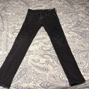 Svarta Replay jeans Anbass 29/32 - Säljer ett par svarta Replay Anbass jeans i storlek 29/32. Jeansen har en slim passform med klassisk femficksdesign och snygga detaljer som Replay-logga på fickan. Materialet är jeans och färgen är mörk svart, perfekt för en stilren look. Andvända max 5-10 gånger köpta på replays offensiela sida kan leta fram kvitto samt order bekräftelse om de skulle behövas. 