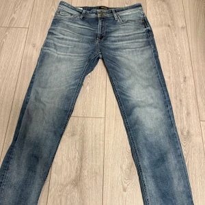 Jack & Jones Regular Clark jeans blå - Snygga blå jeans från Jack & Jones, modell Regular Clark. Klassisk femficksdesign med normal passform och raka ben. Jeansen har en tvättad look med ljusare partier och är tillverkade i slitstarkt denimtyg.
