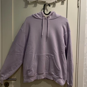 Ljuslila hoodie från Monki - Supermjuk ljuslila hoodie från Monki i oversized modell. Tröjan har huva med snörning, stor magficka och ribbade muddar. Perfekt för chill dagar och enkel att styla med jeans eller leggings.