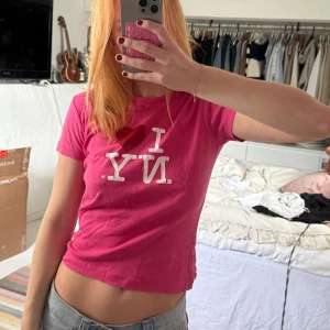 Rosa I ❤️ NY t-shirt croppad - Säljer en rosa croppad t-shirt med det klassiska I ❤️ NY-trycket framtill. T-shirten har korta ärmar och en figurnära passform. Perfekt för dig som gillar statement-plagg och vill sticka ut med en färgstark look.