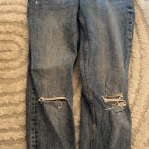 Ljusblå ripped jeans från Zara - Säljer ett par ljusblå jeans från Zara med slitna detaljer och hål vid knäna. Jeansen har klassisk femficksdesign, normal passform och är tillverkade i bomull. Perfekta för en avslappnad och trendig look.