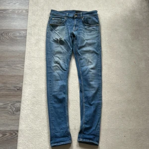 Slim jeans från Tiger of Sweden - Snygga blå slim fit jeans från Tiger of Sweden, tillverkade i Italien. Jeansen har klassisk femficksdesign, smal passform och subtila slitningar framtill. Perfekta för dig som gillar en stilren och modern look.
