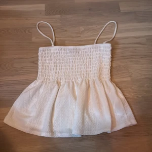 Vit smockad linnetopp Gina Tricot XS - Supersöt vit linnetopp från Gina Tricot i storlek XS. Toppen har smockad överdel, tunna axelband och en lätt utställd nederdel. Materialet är mjukt och har en lätt struktur som ger en chill och feminin vibe. Perfekt för varma dagar och snygg att styla med jeans eller kjol. Kan ta av axelbandet och sätta som en vit kjol om man vill de också! 