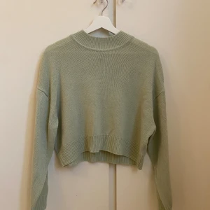 Ljusgrön stickad croppad tröja - Superfin ljusgrön stickad tröja med croppad passform och bred ribbad kant vid hals, ärmslut och nederkant. Perfekt för lager-på-lager och chill dagar. Enkel och stilren design som är lätt att matcha.