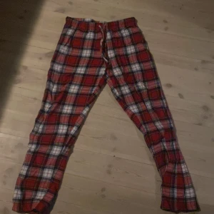 Rödrutiga mjukisbyxor med snörning - Mysiga mjukisbyxor i röd, vit och svart rutig design. Byxorna har resår i midjan och snörning för extra komfort. Perfekta för chill dagar hemma eller som pyjamasbyxor.