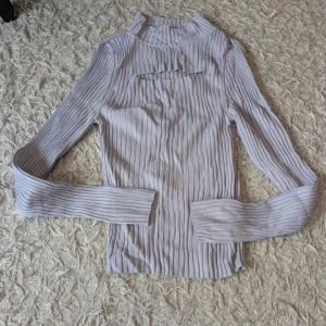 Ljuslila ribbad tröja från Gina Tricot - Trendig ljuslila ribbad tröja från Gina Tricot med lång ärm och hög hals. Tröjan har en snygg cut-out detalj framtill och är figurnära i modellen. Perfekt att styla med jeans eller kjol för en cool look.