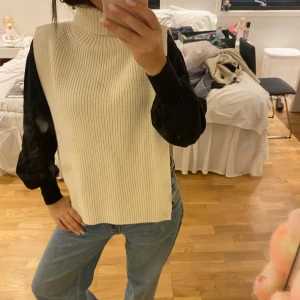 Stickad offwhite slipover från H&M - Säljer en chunky stickad slippover i offwhite från H&M. Modellen är ärmlös med hög krage och har en rak, loose fit med slitsar i sidorna. Perfekt att slänga över en skjorta eller långärmad tröja för en trendig lager-på-lager-look. Kom med bud!