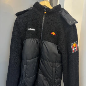  Ellesse Sparra Vinterjacka svart  - Svart jacka från Ellesse i storlek M med teddyfleece upptill och quiltad puffer nedtill. Jackan har huva, dragkedja framtill och Ellesse-loggor på bröstet och ärmen. Snygg mix av material och detaljer som ger en cool streetstil. Kan gå ner i pris vid snabb affär 