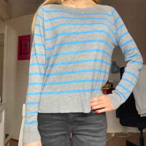 Gråblå randig stickad tröja - Säljer en stickad tröja i grått med blå ränder. Tröjan har en rak passform, rund halsringning och långa ärmar. Perfekt för dig som gillar en enkel men snygg stil. Supermjuk och skön att ha på sig.  Är lite noppig som ni ser på andra bilden.