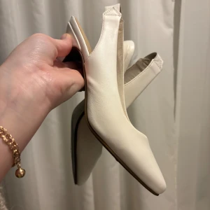  klackskor - Snygga vita pumps med låg klack och spetsig tå. Skorna har en öppen häl med elastisk rem för skön passform. Tillverkade i slätt syntetmaterial med en stilren och minimalistisk look. Perfekta för dig som gillar klassisk och clean stil.