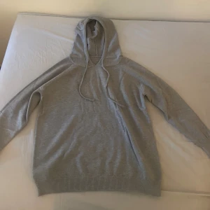 Grå hoodie med huva(cashmere) och snörning - Säljer en enkel och stilren grå hoodie (cashmere) med huva och snörning. Tröjan har långa ärmar och ribbade muddar vid ärmslut och nederkant. Perfekt för en avslappnad look och passar till det mesta.