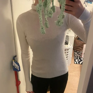 Vit ribbad polotröja - Säljer en vit ribbad polotröja med lång ärm. Tröjan är tight i modellen och har en hög hals som ger en clean och stilren look. Perfekt att matcha med jeans eller kjol för en enkel men snygg outfit.