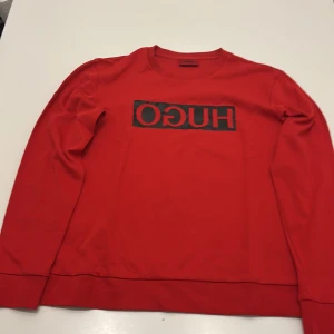 Röd långärmad tröja från Hugo - Röd långärmad tröja från Hugo med svart logga i boxprint över bröstet. Tröjan har ett väldigt skönt material som gör att den sitter perfekt och känns perfekt på dig. Tröjan är äkta och är väldigt fin. Den har storleken L men passar folk som har storleken M också. Pris kan diskuteras.