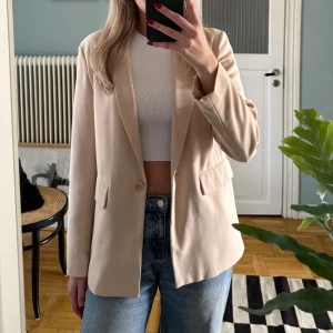 Beige kavaj  - Stilren beige kavaj från NLY Trend med klassisk krage, en knapp framtill och två fickor med lock. Långärmad modell i mjukt material som ger en snygg och clean look.