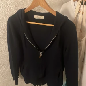 Kashmir hoodie - Mysig svart hoodie från Sayless i lyxig kashmir. Tröjan har dragkedja framtill, huva och långa ärmar. Perfekt för dig som vill ha en stilren och bekväm look med exklusiv känsla.