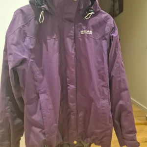Lila vindjacka från 8848 Altitude - Lila vindjacka från 8848 Altitude med huva och justerbara snören. Jackan har dragkedja framtill, långa ärmar och praktiska fickor. 