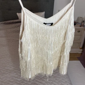 Vit fransig linnetopp från Bik Bok - Säljer en vit linnetopp från Bik Bok i storlek L. Toppen har tunna axelband och är täckt med långa fransar som ger en cool och dansvänlig look. Materialet känns mjukt och lätt, perfekt för att sticka ut med en unik stil. Passar dig som gillar att synas och vill ha något extra.