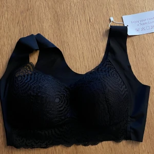 Svart spetsig korsett från Comfit - Säljer en svart korsett-topp från Comfit med snygg spets framtill och breda axelband. Toppen har ett elegant mönster i spetsen och är tillverkad av nylon, spandex, viskos och polyester för en mjuk och stretchig känsla. Perfekt för dig som vill ha en cool och bekväm look.