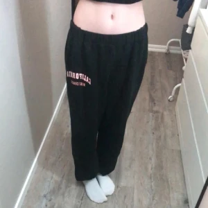 Svarta mjukisbyxor med tryck - Svarta mjukisbyxor med resår i midjan och vid bensluten. Tryck med texten 'California' i vitt och rött på ena benet. Byxorna har en loose passform och är gjorda i mjukt bomullsmaterial, perfekta för chill dagar. Dom är egentligen lite högmidjade