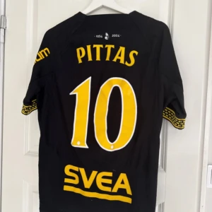AIK matchtröja Nike Dri-Fit M med Pittas tryck - AIK fotbollströja med Pittas 10 på ryggen, tillverkad i svart Dri-Fit polyester. Snygga gula detaljer och tryck, samt AIK-emblem på bröstet. Kortärmad modell med mönstrade muddar och slim fit-passform. Perfekt för dig som vill representera AIK på läktaren eller träningen.