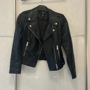 Svart skinnjacka Vero Moda M - Snygg svart skinnjacka från Vero Moda i storlek M. Med silvriga dragkedjor, knappar, detaljer på axlarna och två fickor med dragkedja framtill.       Liten i storleken! Säljer pågrund av att den är för liten! Endast använd fåtal gånger.