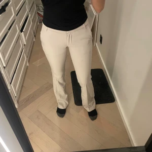 Beiga kostymbyxor från BikBok, strl 34 - Snygga beiga kostymbyxor från BikBok i storlek 34. Byxorna har hög midja, raka ben med lätt bootcut och klassiska fickor både fram och bak. 