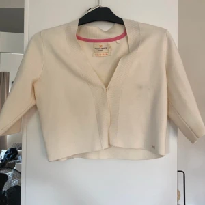 Vit kofta från Holly & Whyte - Snygg vit kofta från Holly & Whyte by Lindex med trekvartsärm och croppad passform. Koftan har ribbade detaljer vid halsringningen och är tillverkad i mjukt material. Perfekt att slänga över en topp för en clean look.