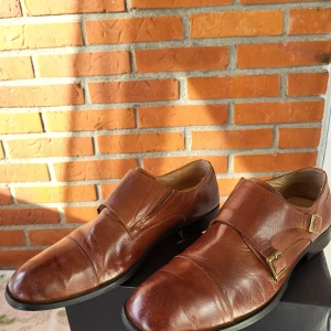 Bruna skinnloafers från Dahlin strl 43 - Snygga bruna loafers från Dahlin i äkta skinn med dubbla spännen i guldton. Klassisk design med rund tå och platt sula, perfekt för dig som gillar stilrena och tidlösa skor. Passar dig som vill ha en dressad look med lite edge.