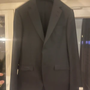 Svart klassisk kavaj herr - Stilren svart tiger of sweden kavaj med klassisk passform och två framfickor med lock. Enkelknäppt och med snyggt skurna slag. Perfekt för dig som vill ha en tidlös look till kostymen.